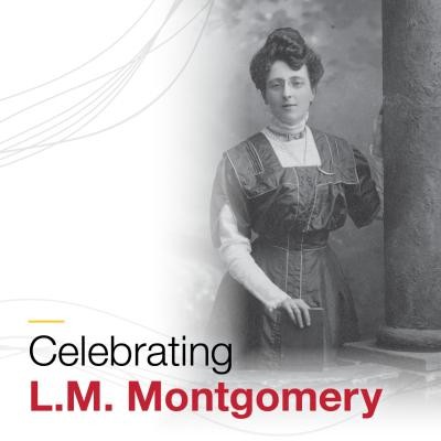 L.M. Montgomery standing holding a book on a tabletop.