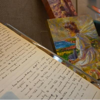 A close up of the L.M. Montgomery's first journal (Sept. 21, 1889 - Apr. 19, 1897) and her 2 painted studies in the background. 